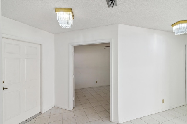 empty room with light tile patterned floors, visible vents, a chandelier, and a textured ceiling