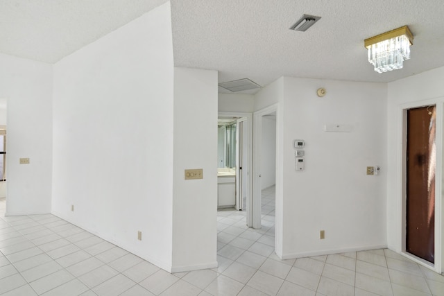 spare room featuring light tile patterned floors, visible vents, a chandelier, and a textured ceiling