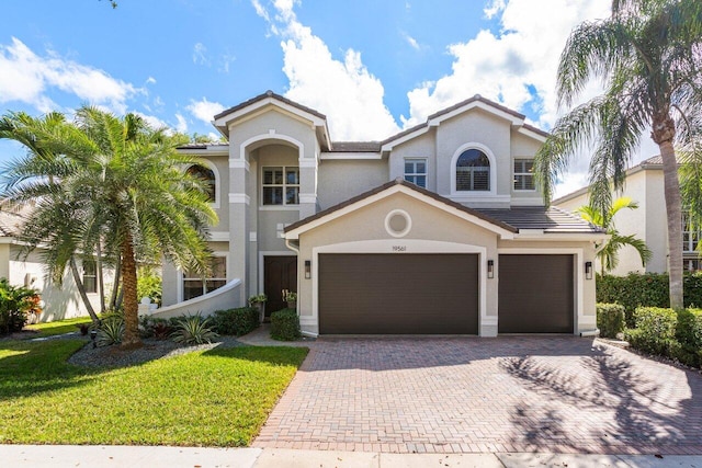 mediterranean / spanish-style home with a garage, a front lawn, decorative driveway, and stucco siding