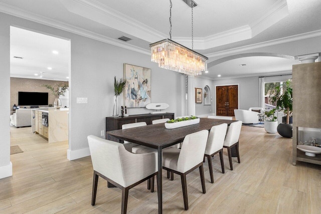 dining area featuring arched walkways, crown molding, a raised ceiling, visible vents, and light wood-type flooring