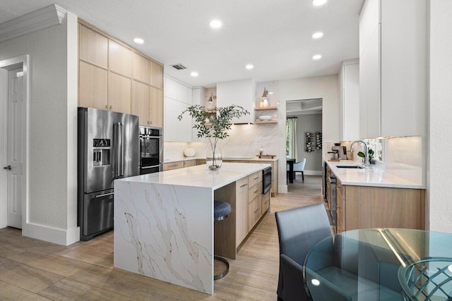 kitchen with light brown cabinets, a kitchen island, a sink, appliances with stainless steel finishes, and open shelves