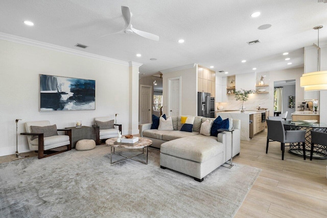 living room with ornamental molding, visible vents, light wood-style floors, and ceiling fan