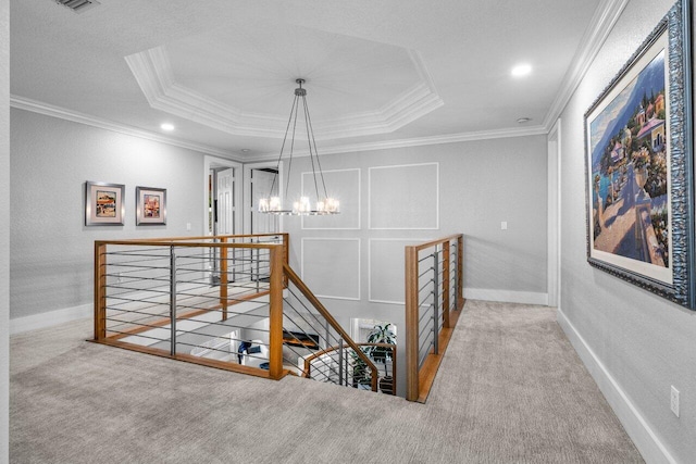 corridor featuring carpet flooring, an upstairs landing, ornamental molding, a tray ceiling, and an inviting chandelier