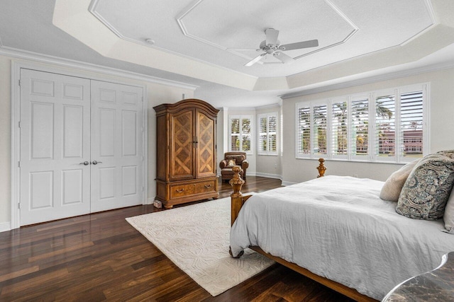 bedroom featuring crown molding, dark wood finished floors, a raised ceiling, a closet, and a ceiling fan