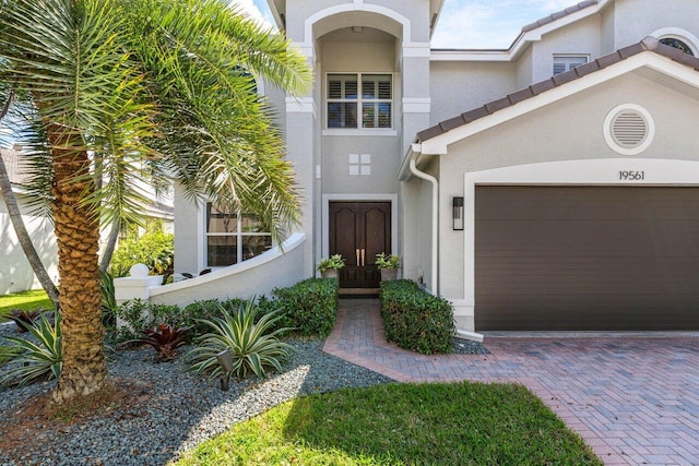 doorway to property with a garage, a tiled roof, decorative driveway, and stucco siding