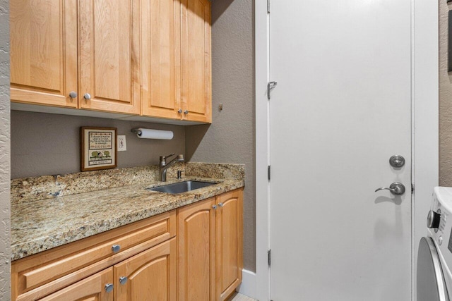 kitchen featuring washer / dryer, a sink, and light stone countertops