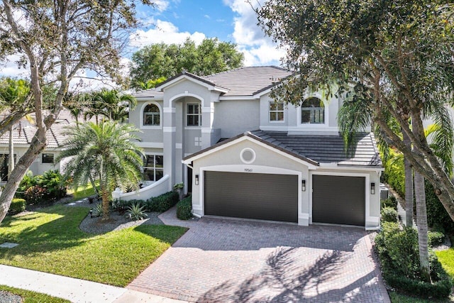 mediterranean / spanish house with decorative driveway, a front yard, a tile roof, and stucco siding