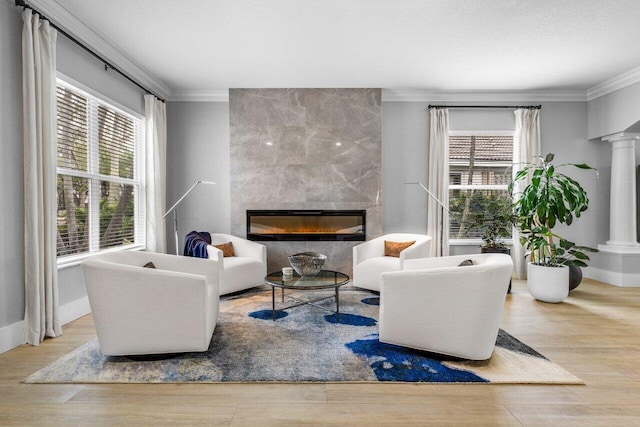 living area featuring ornate columns, a fireplace, ornamental molding, and wood finished floors