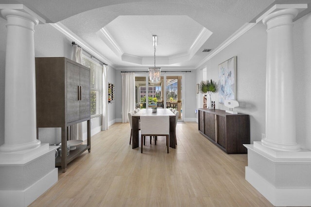 dining room with light wood-type flooring, decorative columns, and a raised ceiling