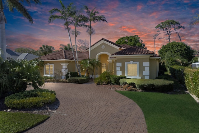 mediterranean / spanish house featuring stucco siding, a tiled roof, decorative driveway, and a front yard