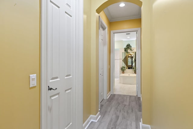 corridor with ornamental molding, light wood-style floors, arched walkways, and baseboards