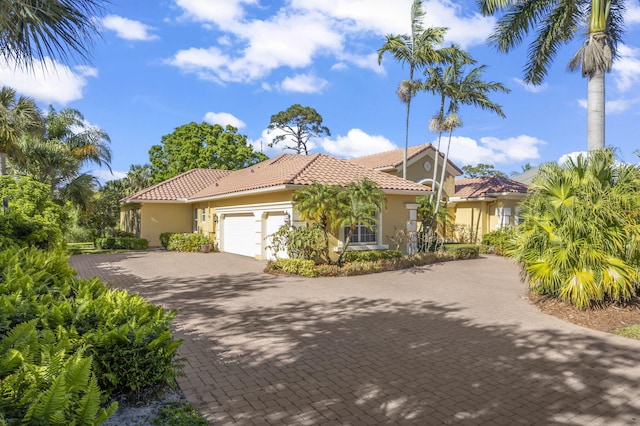 mediterranean / spanish-style home with stucco siding, an attached garage, a tile roof, and decorative driveway