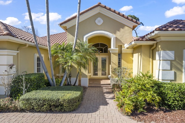 view of exterior entry featuring french doors, stucco siding, and a tile roof