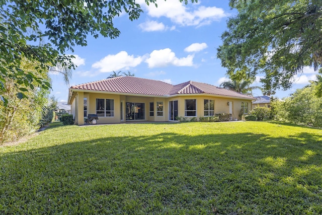 back of property with stucco siding, a lawn, and a tile roof