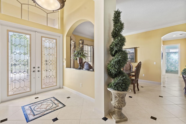 tiled entryway with baseboards, arched walkways, french doors, and ornamental molding