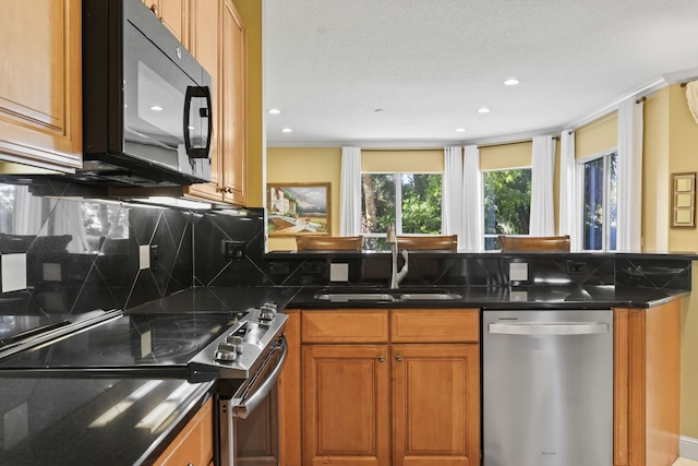 kitchen with brown cabinets, a sink, dark stone countertops, appliances with stainless steel finishes, and decorative backsplash