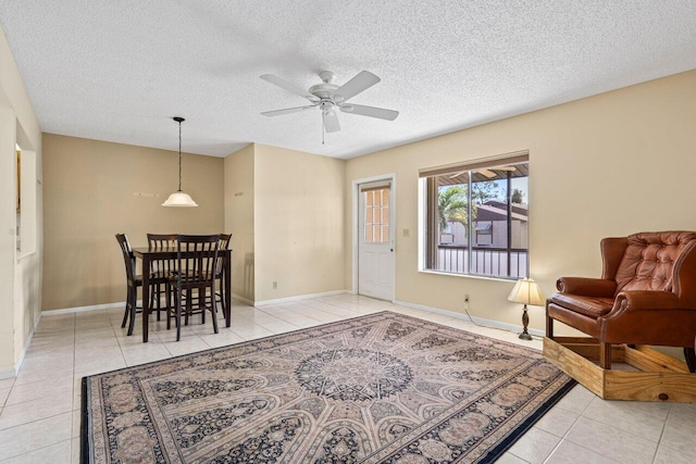 living area with a ceiling fan, light tile patterned flooring, a textured ceiling, and baseboards