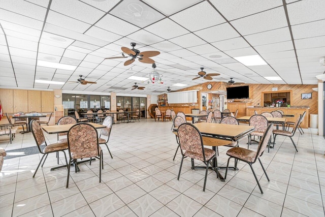 dining room with a paneled ceiling, wood walls, and light tile patterned floors