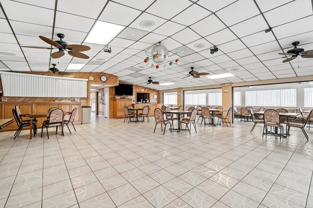 unfurnished dining area with ceiling fan, plenty of natural light, a paneled ceiling, and wooden walls