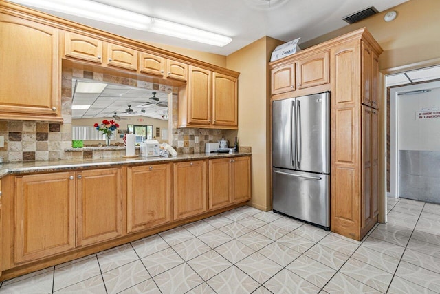 kitchen featuring visible vents, light stone counters, freestanding refrigerator, and decorative backsplash