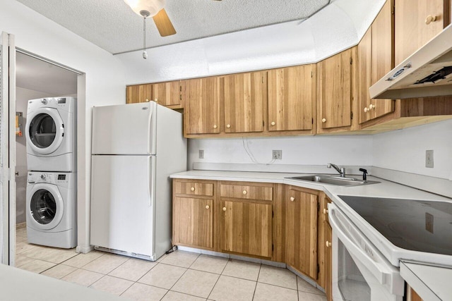 kitchen with white appliances, light tile patterned floors, stacked washer / drying machine, light countertops, and under cabinet range hood