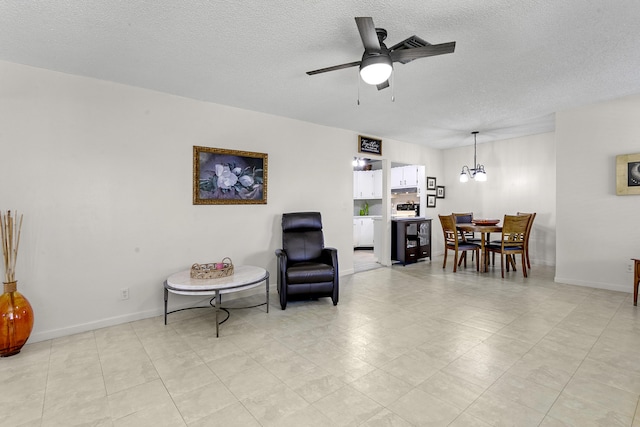 sitting room with a textured ceiling, baseboards, and ceiling fan with notable chandelier