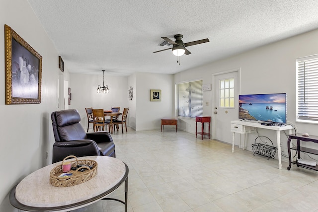 living room featuring ceiling fan with notable chandelier and a textured ceiling