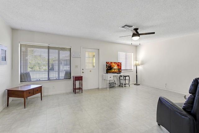 sitting room with a textured ceiling, baseboards, visible vents, and a ceiling fan