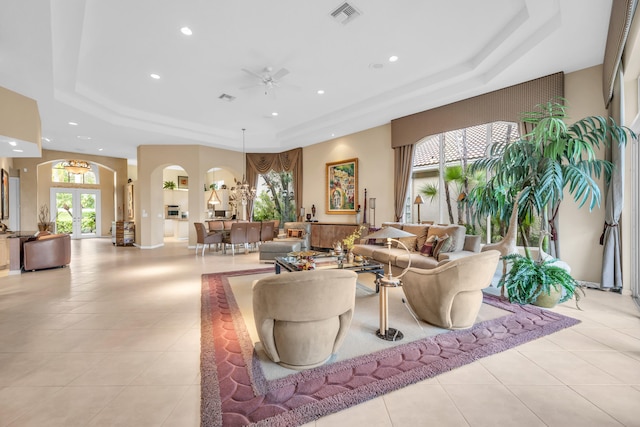 living area with visible vents, a tray ceiling, arched walkways, and light tile patterned flooring