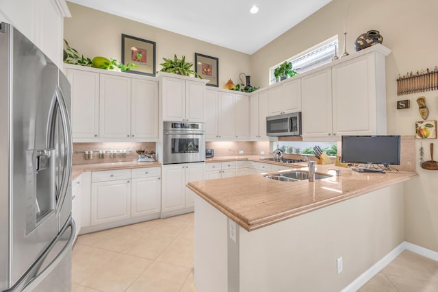 kitchen featuring light tile patterned floors, stainless steel appliances, a peninsula, white cabinetry, and backsplash