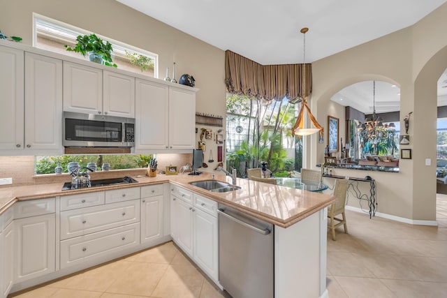 kitchen featuring decorative backsplash, a peninsula, stainless steel appliances, a sink, and light tile patterned flooring