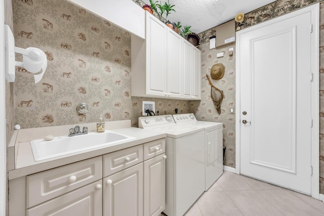 clothes washing area featuring wallpapered walls, washing machine and dryer, cabinet space, and a sink