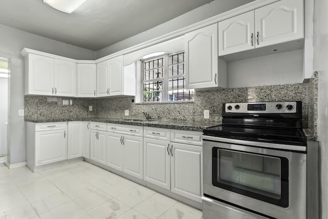 kitchen featuring backsplash, dark stone counters, stainless steel range with electric stovetop, white cabinetry, and a sink