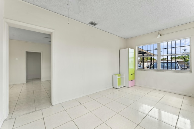 empty room featuring light tile patterned flooring, baseboards, visible vents, and a textured ceiling