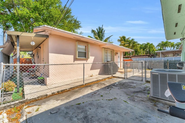 view of side of home featuring a gate, fence, central AC, and stucco siding