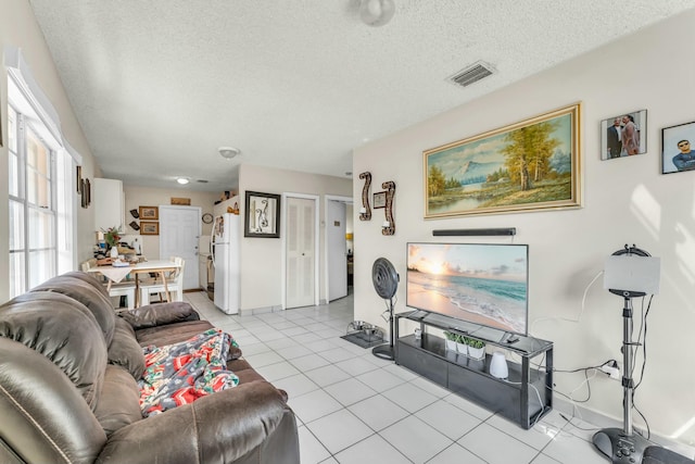 living area with light tile patterned flooring, visible vents, a textured ceiling, and baseboards