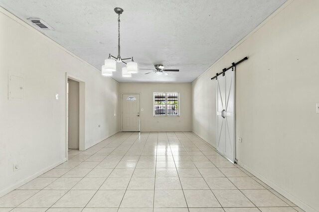 unfurnished room featuring a barn door, light tile patterned floors, ceiling fan with notable chandelier, and visible vents