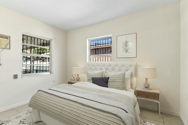 bedroom with an AC wall unit, light tile patterned flooring, and baseboards