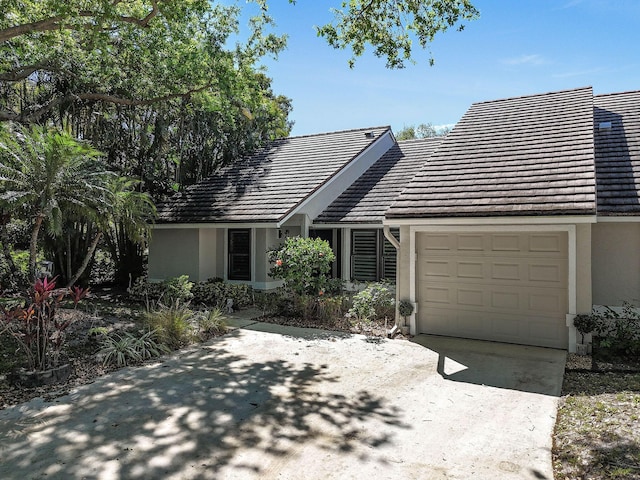 view of front of house with driveway, an attached garage, a tiled roof, and stucco siding