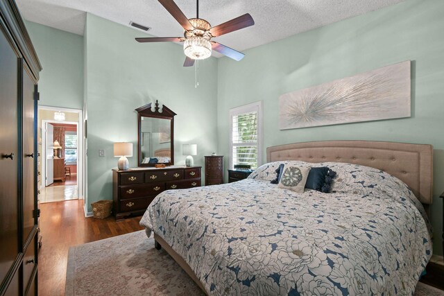 bedroom with a textured ceiling, a high ceiling, wood finished floors, visible vents, and a ceiling fan