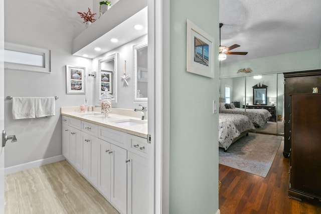 ensuite bathroom featuring baseboards, ensuite bath, ceiling fan, wood finished floors, and a sink