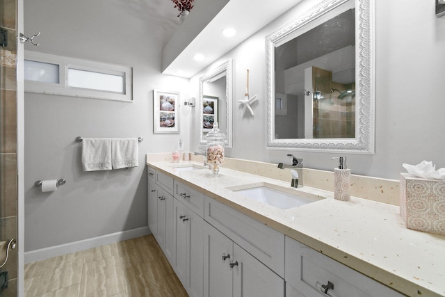 bathroom featuring double vanity, a stall shower, a sink, and baseboards