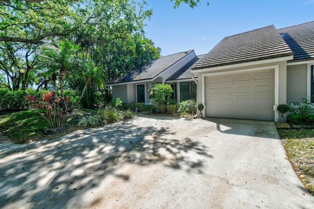 view of front of property featuring concrete driveway, a tiled roof, an attached garage, and stucco siding