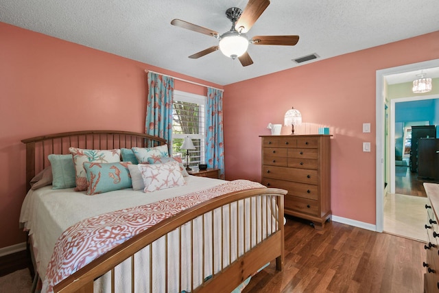 bedroom with a textured ceiling, ceiling fan, wood finished floors, visible vents, and baseboards