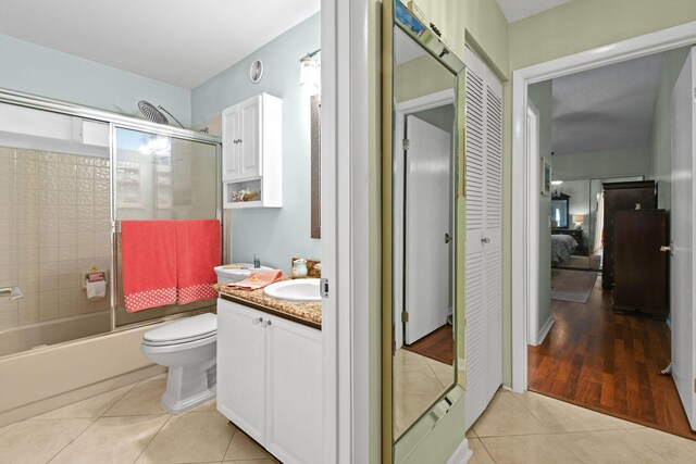 bathroom featuring tile patterned flooring, combined bath / shower with glass door, vanity, and toilet