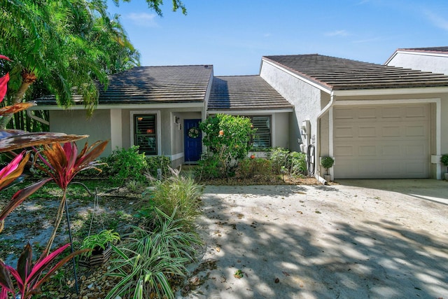 mid-century modern home featuring concrete driveway, a tiled roof, an attached garage, and stucco siding