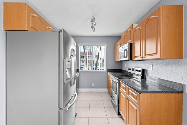 kitchen featuring light tile patterned floors, stainless steel appliances, rail lighting, a textured ceiling, and baseboards