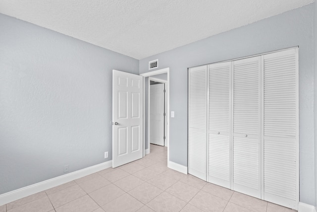 unfurnished bedroom featuring light tile patterned floors, a closet, visible vents, a textured ceiling, and baseboards