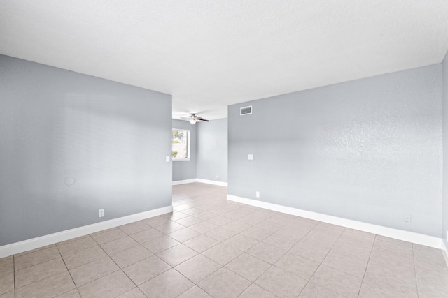 tiled empty room featuring visible vents, ceiling fan, and baseboards