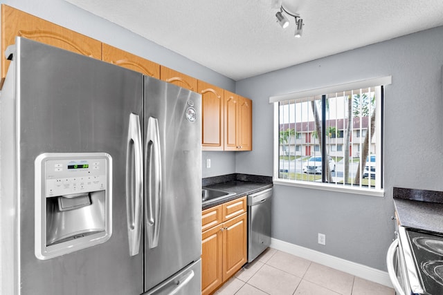 kitchen featuring light tile patterned floors, a textured ceiling, stainless steel appliances, baseboards, and dark countertops